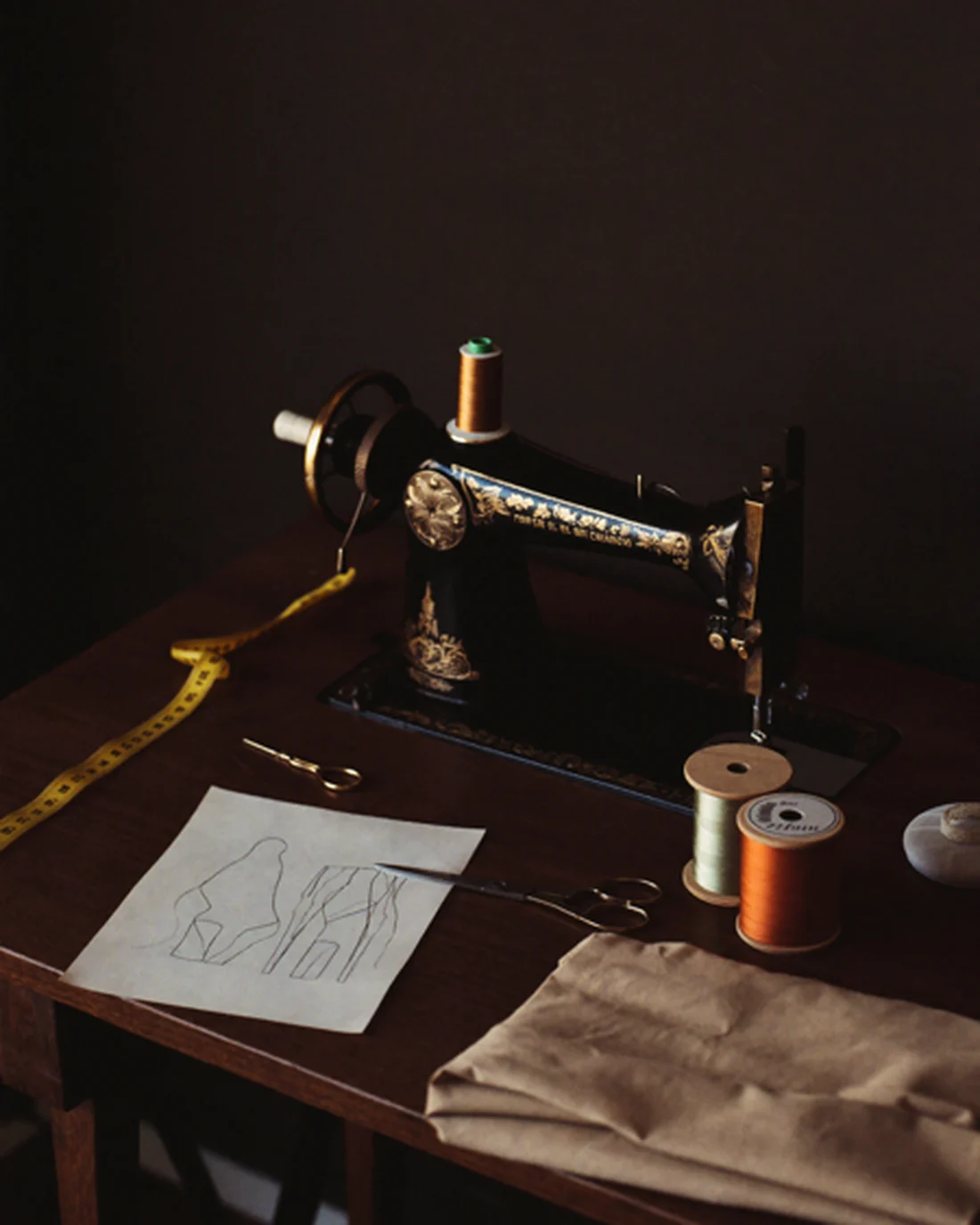 Il banco da lavoro dell'atelier: una macchina da cucire d'epoca, il metro da sarta, le forbici, un bozzetto e i rocchetti di filo