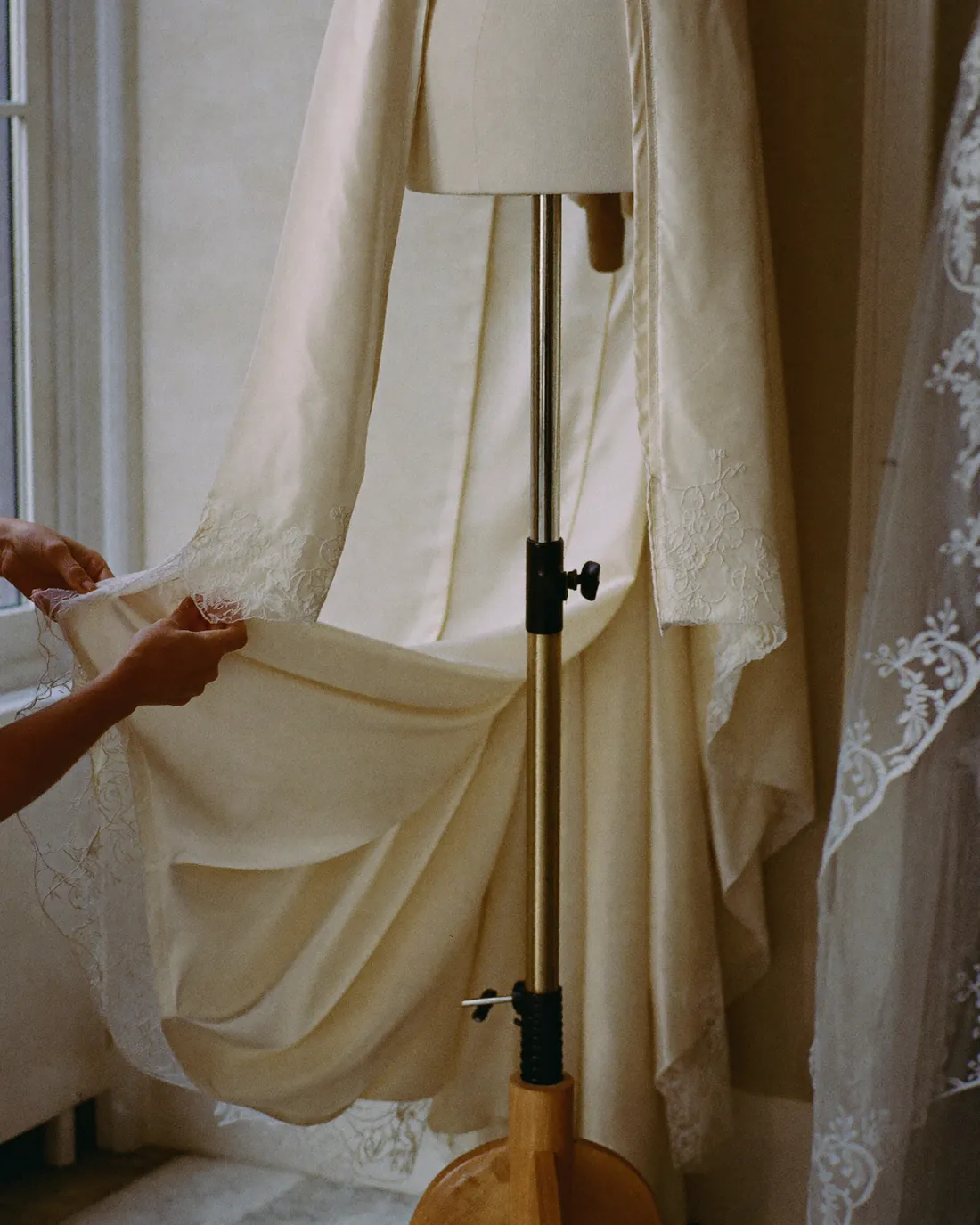 Un abito da sposa in seta e pizzo avorio sul manichino da sartoria, con l'orlo appuntato a mano